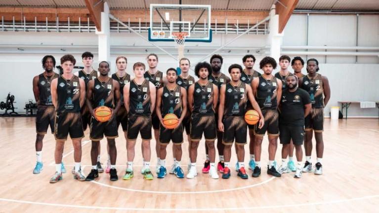 Basketballmannschaft in schwarzer Spielkleidung steht in einer Halle vor dem Korb