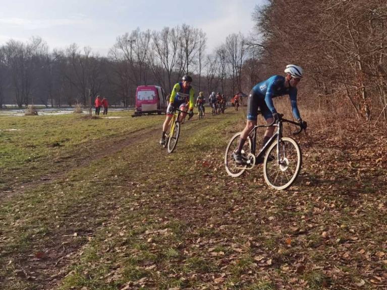 Mehrere Radfahrer fahren auf einem schmalen Waldweg entlang einer Wiese.