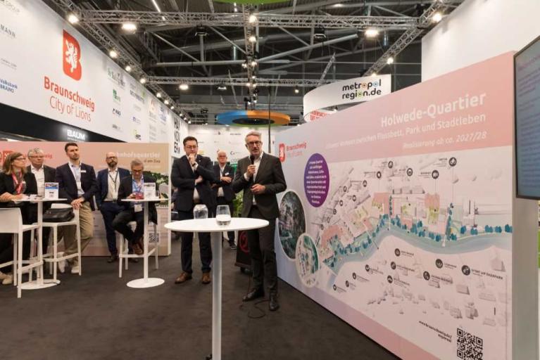 Messestand mit mehreren Personen und einer Präsentation zum Holwedde-Quartier in Braunschweig