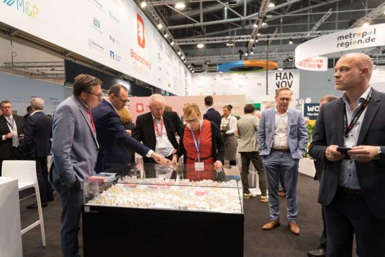 Mehrere Personen auf einer Messe betrachten gemeinsam ein Modell in einer Glasvitrine