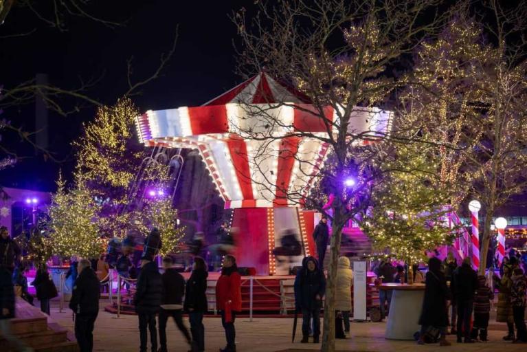 Weihnachtsmarkt bei Nacht mit beleuchtetem Karussell und geschmückten Bäumen